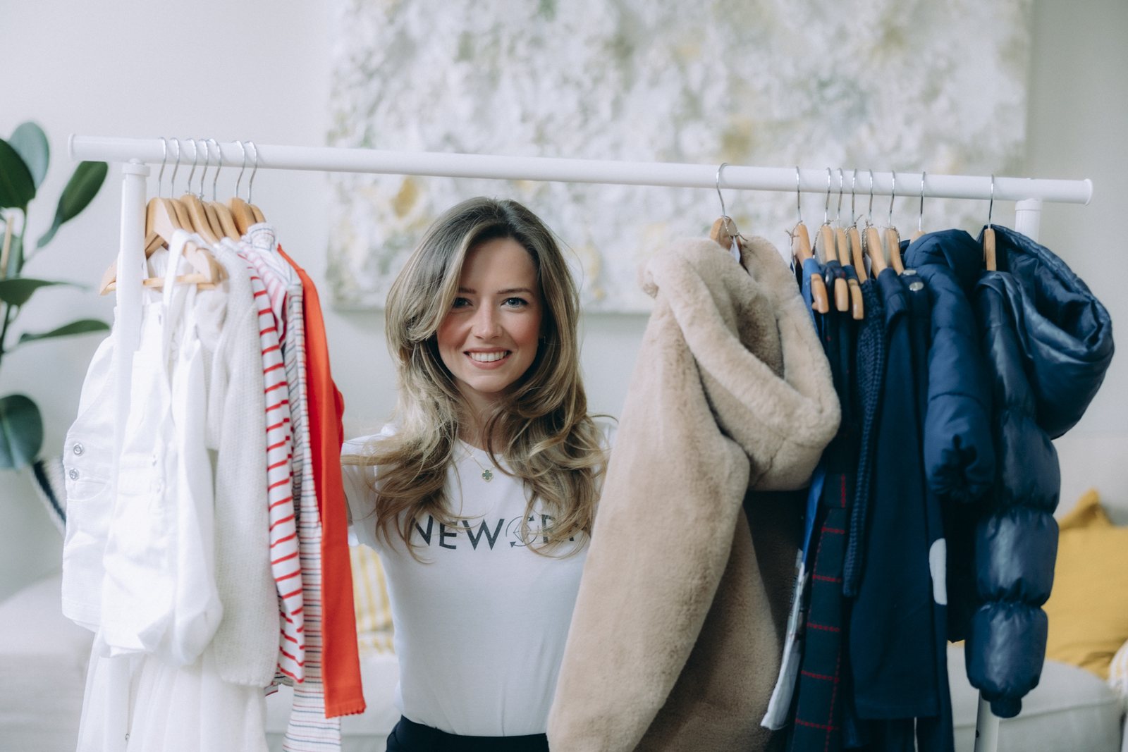 Die Gründerin von Neworn steht lächelnd hinter einer Kleiderstange mit Second-Hand-Kinderkleidung.